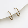 A pair of textured gold hoop earrings displayed on a minimalist white card against a clean white background.
