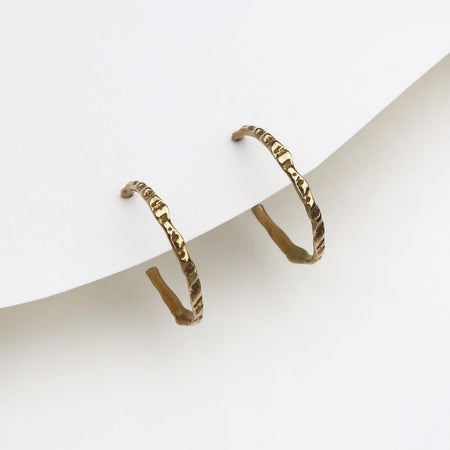 A pair of textured gold hoop earrings displayed on a minimalist white card against a clean white background.