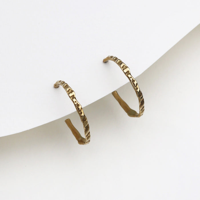 A pair of textured gold hoop earrings displayed on a minimalist white card against a clean white background.