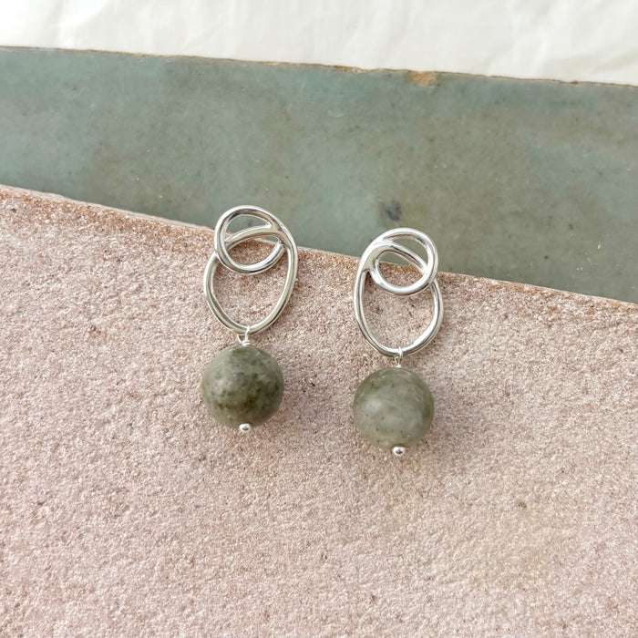Silver earrings with green beads on a stone surface
