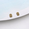 A pair of small gold stud earrings with a textured, ribbed design, displayed on a white card against a light blue background.