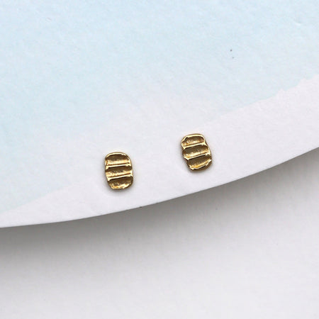 A pair of small gold stud earrings with a textured, ribbed design, displayed on a white card against a light blue background.