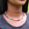 Necklace with multicolored beads worn by a person against a neutral background
