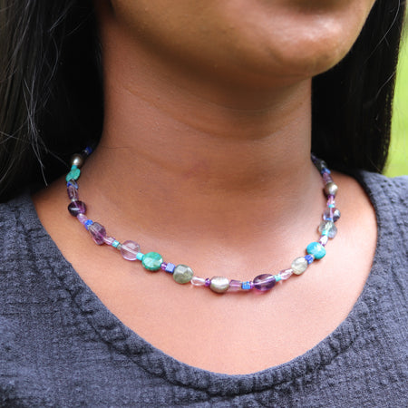 Necklace with multicolored beads worn by a person against a neutral background